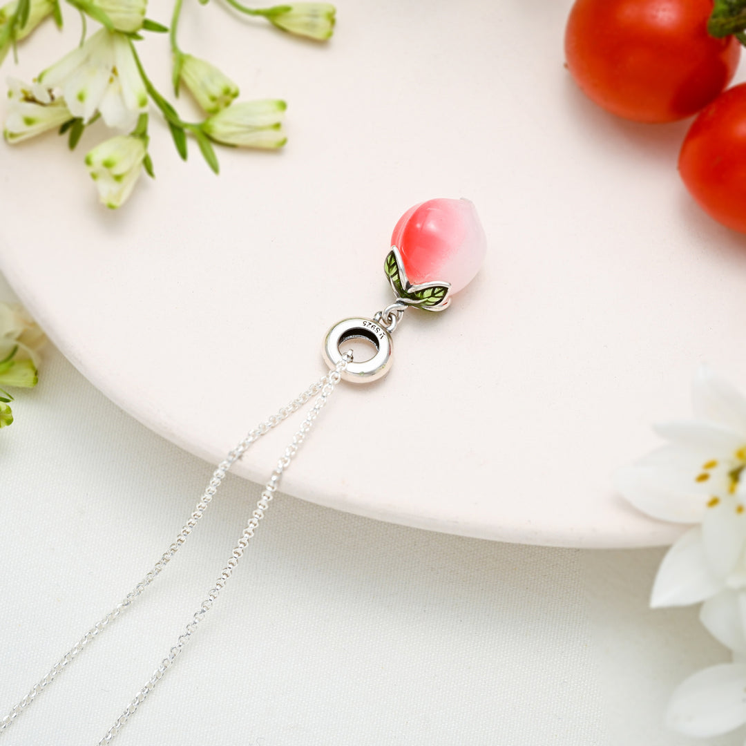 Flat lay of silver peach pendant necklace placed on a white plate with flower accents and tomatoes