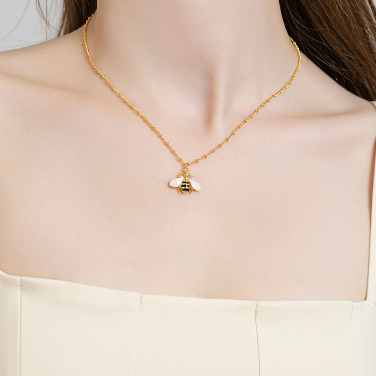 Close-up of woman wearing a delicate gold bee pendant necklace with pink wings and fine chain detail