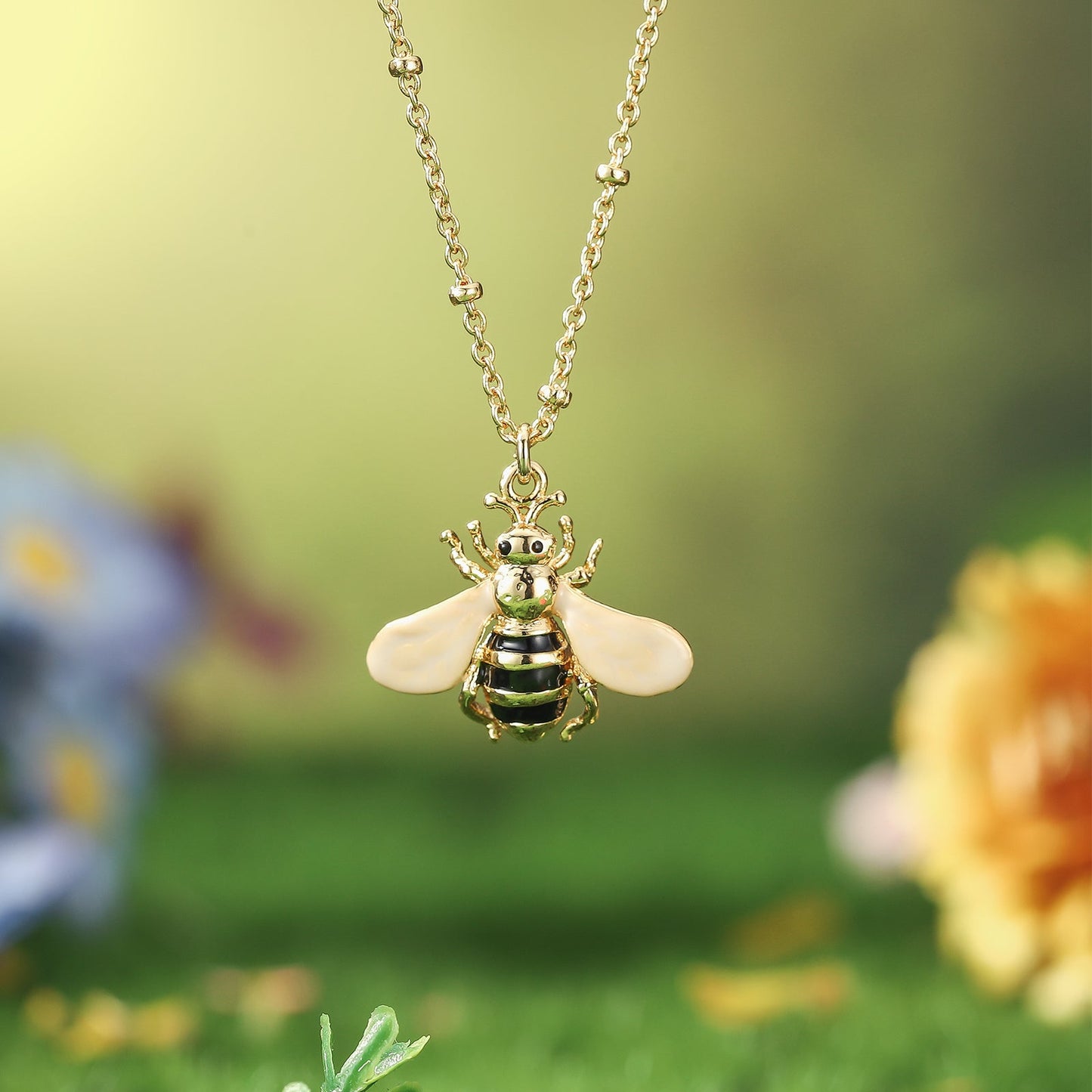 Detailed bee pendant necklace featuring pink wings and striped body, displayed outdoors with floral background