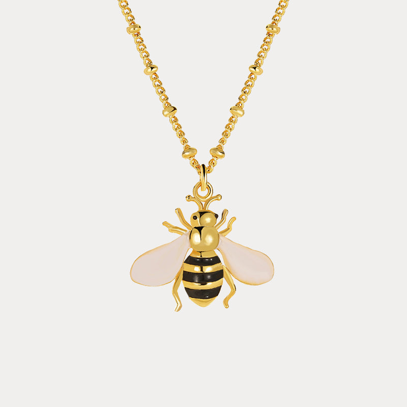 Zoomed-in view of bee pendant with black and gold stripes and soft pink wings, hanging from textured gold chain