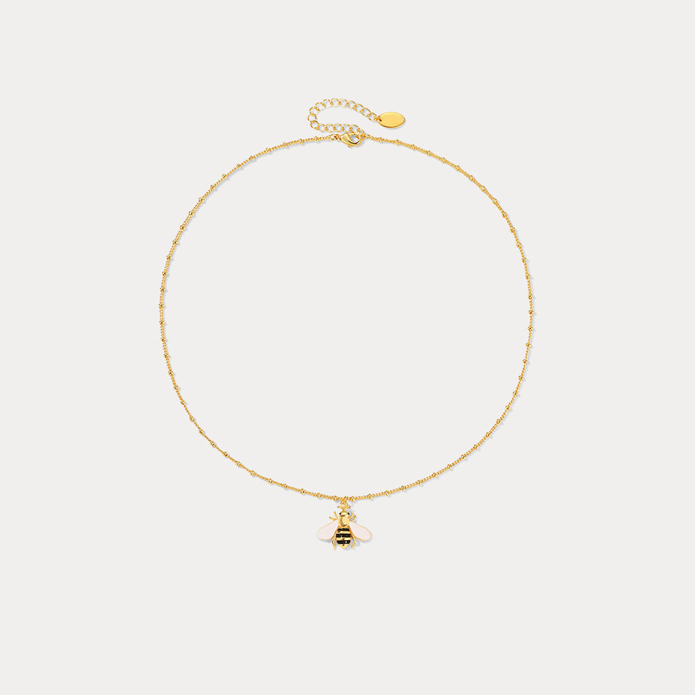 Flat lay of full bee pendant necklace with fine beaded gold chain and small bee charm on white background