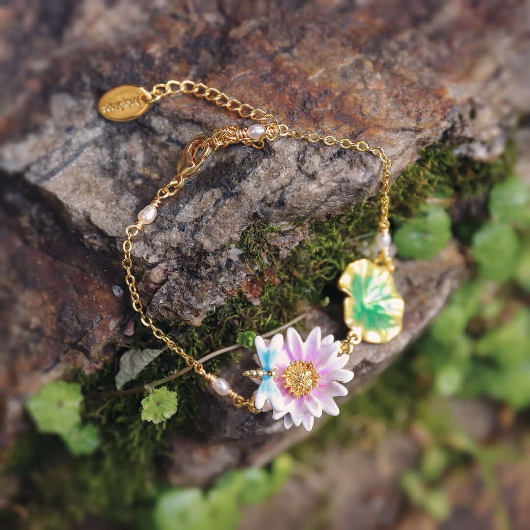 Lotus dragonfly bracelet placed on mossy stone background, featuring pink lotus enamel flower and golden leaf charm.