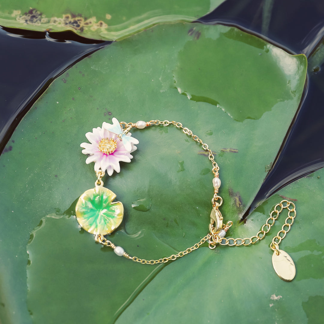 Enamel lotus bracelet displayed on lily pad, showing gold chain, lotus flower charm, and green enamel leaf detail.