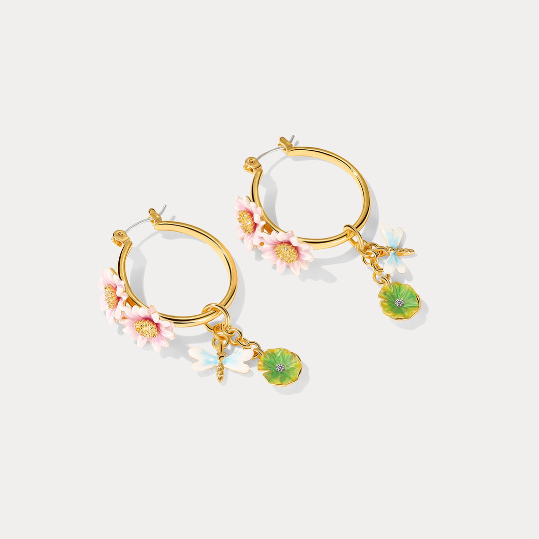 A pair of gold hoop earrings adorned with pink lotus flowers and dangling dragonfly and lily pad charms, displayed on a white background.