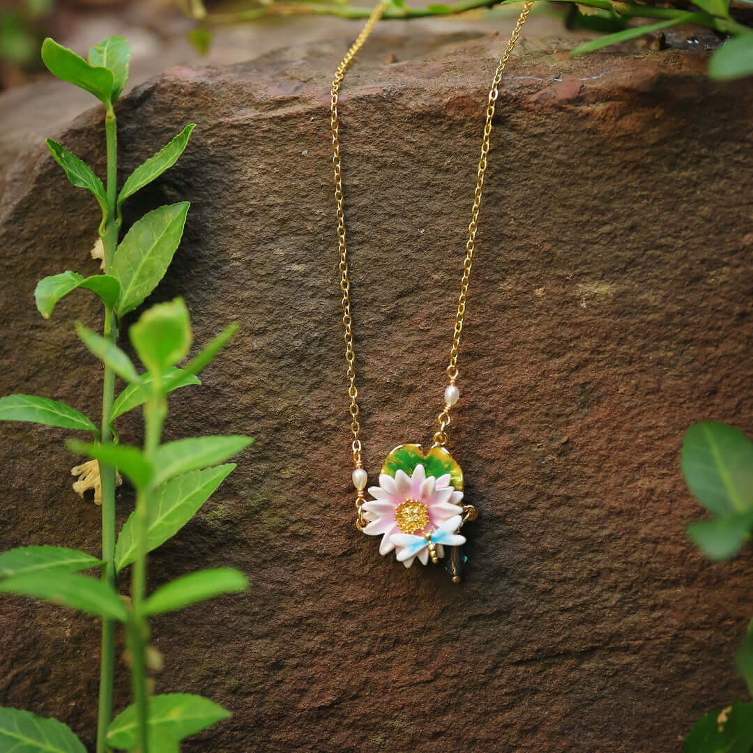 Lotus dragonfly necklace with pearl and enamel charm styled on rustic red rock with green foliage.