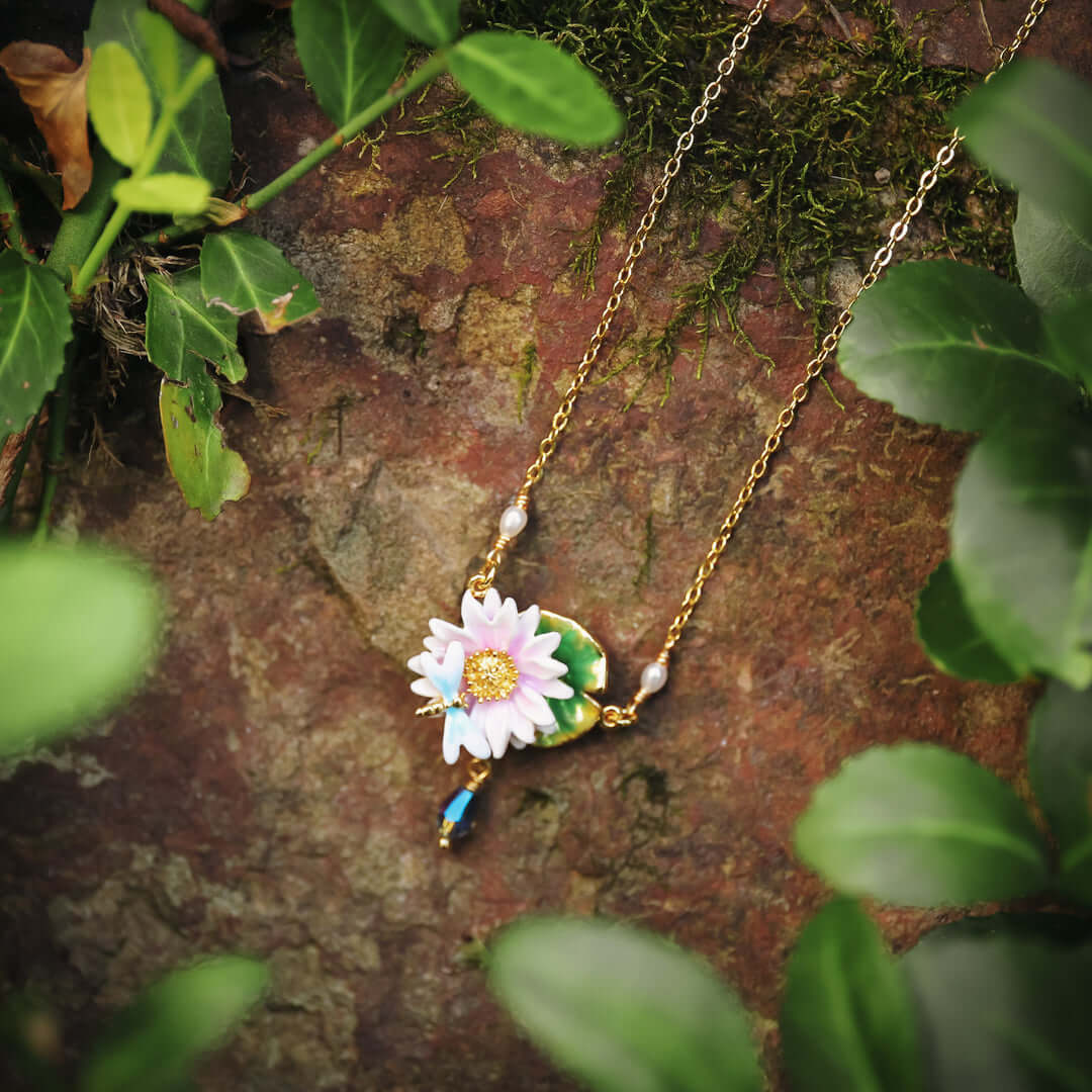 Lotus dragonfly necklace styled outdoors on a stone with green leaves, highlighting botanical theme and pink lotus design.