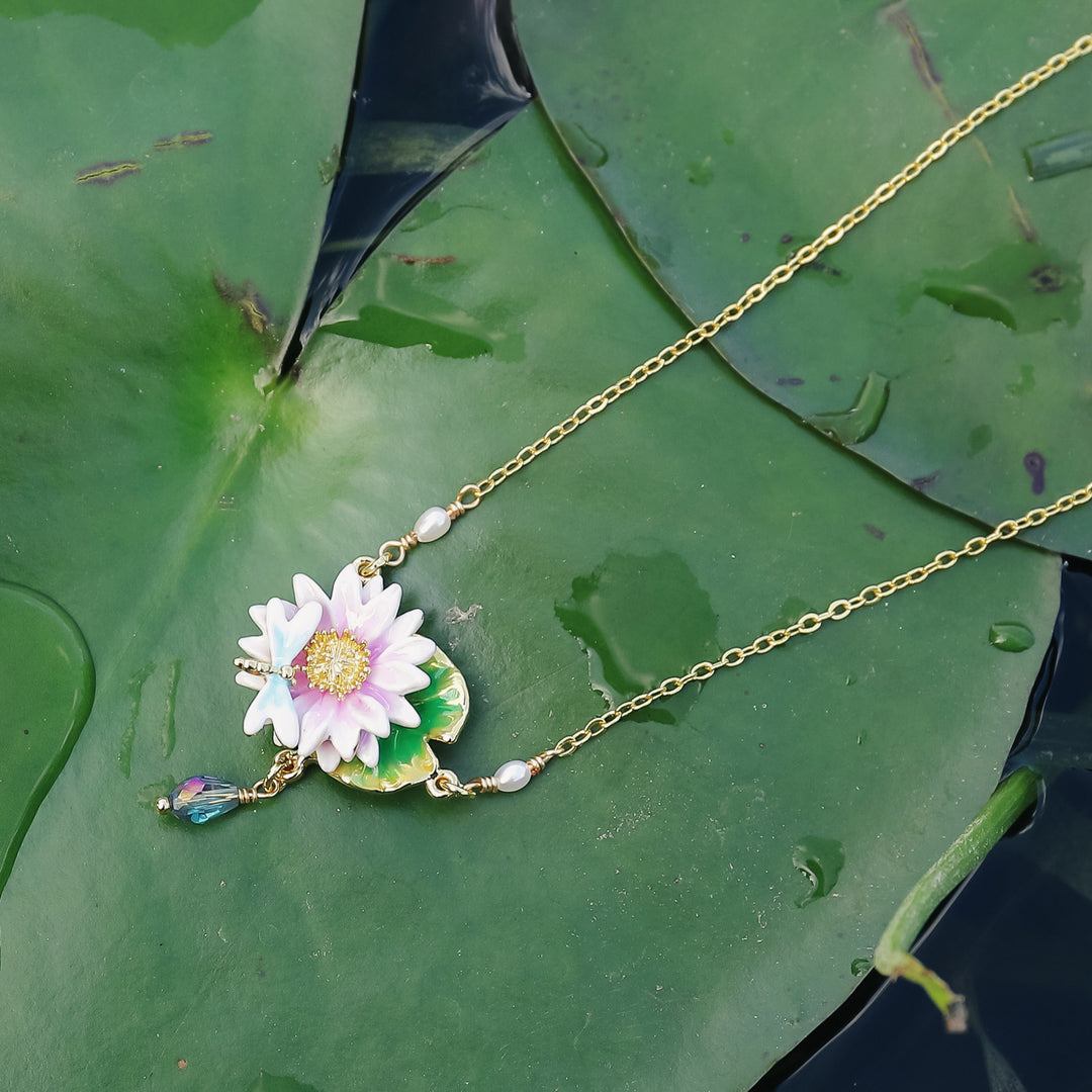 Gold lotus dragonfly necklace displayed on green lily pad, featuring enamel lotus flower, dragonfly charm, and pearl accents.