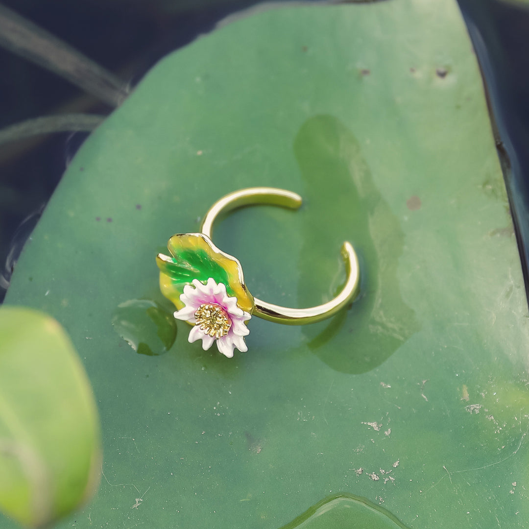 Lotus flower ring placed on a green lily pad, showcasing enamel flower and leaf design.