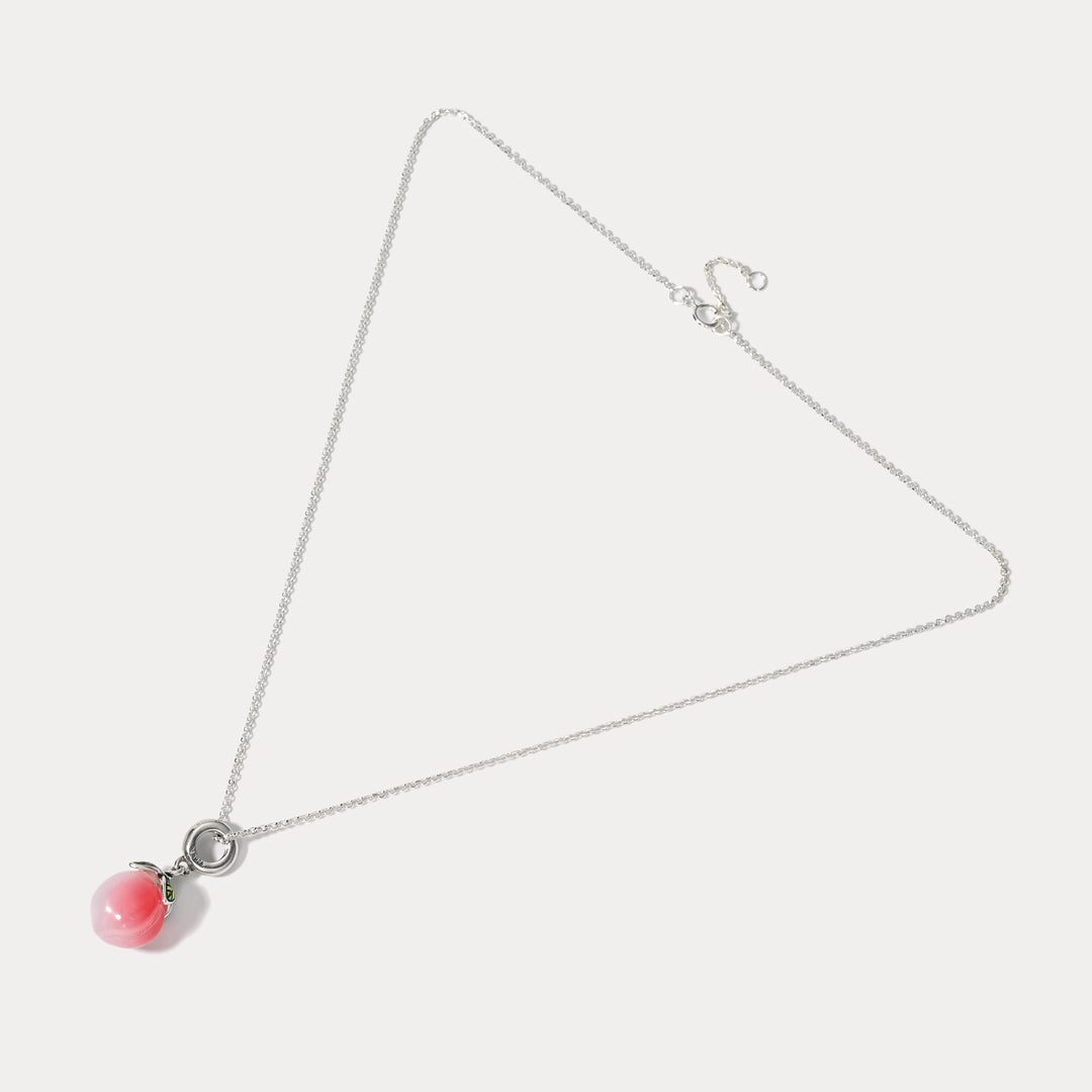 Full view of silver necklace featuring a pink peach-shaped pendant with green enamel leaves on white background