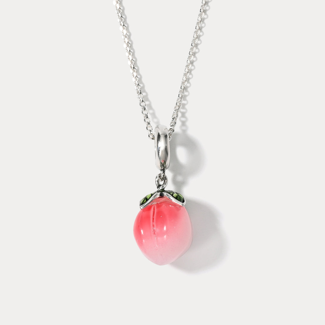 Centered image of glass peach pendant hanging from a fine silver chain, featuring leaf details