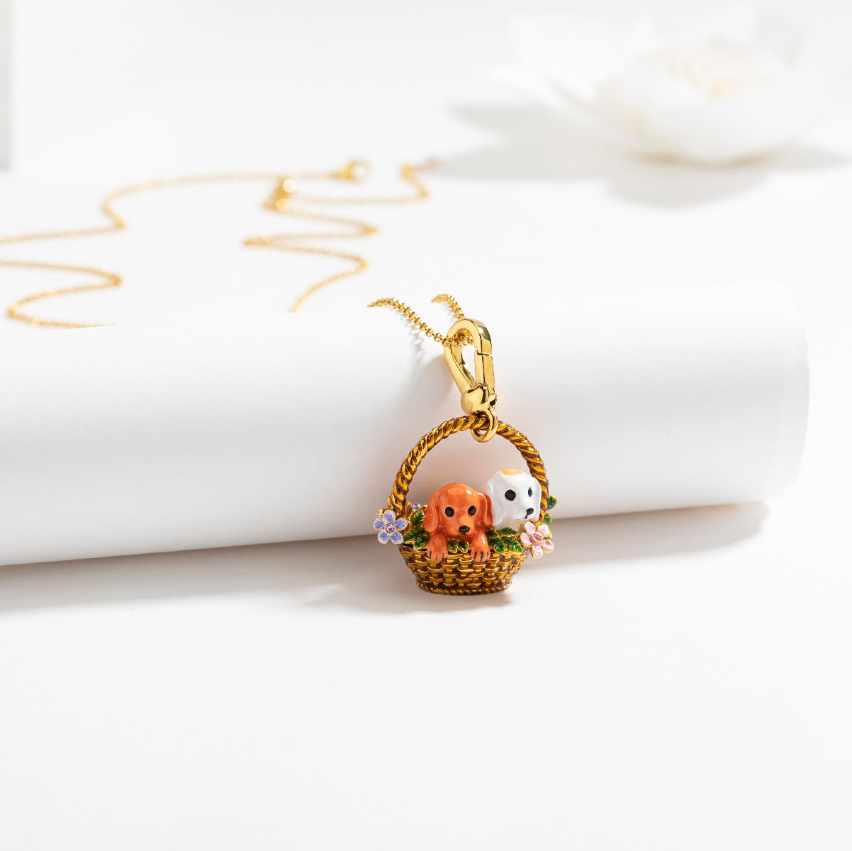 Styled flat lay of the Puppy Locket Pendant Necklace, showing the delicate enamel dog charm in a basket with floral accents.
