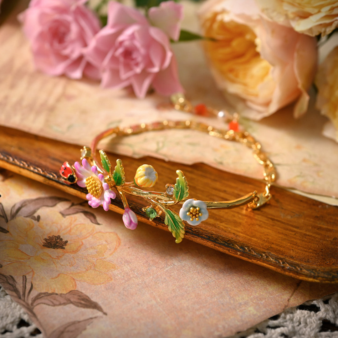Daisy Ladybug Bracelet styled among pink and yellow roses on a decorative wooden tray