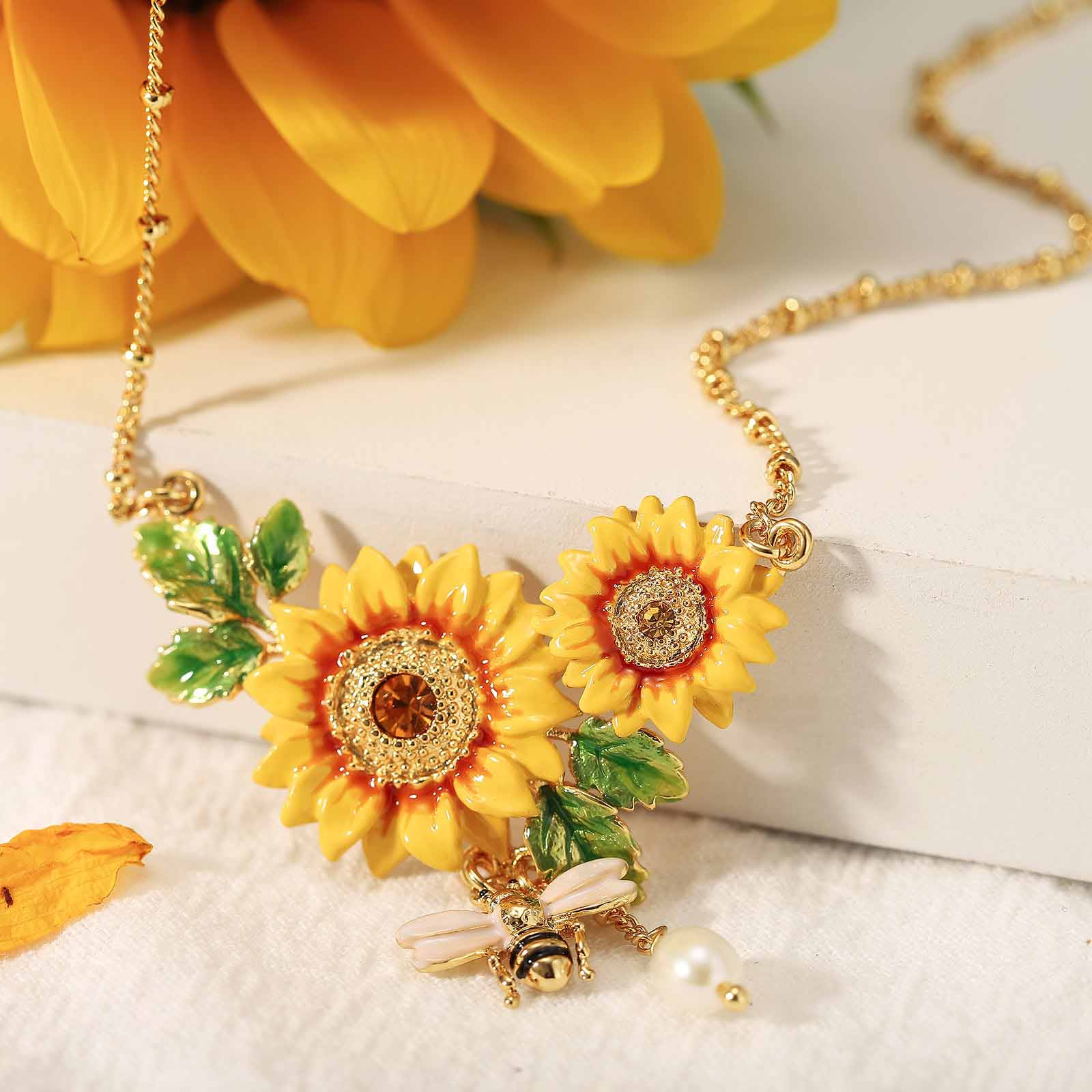 Zoomed view of necklace centerpiece showing enamel sunflowers, leaves, and bee with pearl drop