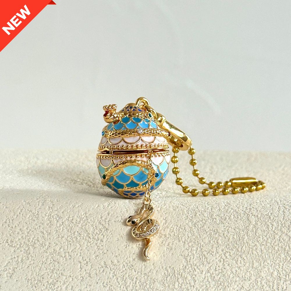 Snake-themed blue enamel egg locket with snake charm emerging, lying on fabric surface