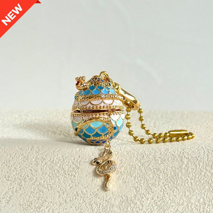 Snake-themed blue enamel egg locket with snake charm emerging, lying on fabric surface