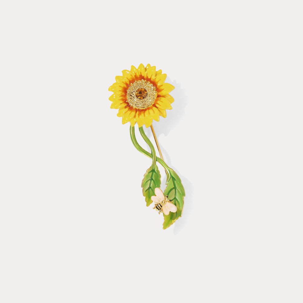 Close-up product shot of sunflower brooch with detailed gold petals, green leaves, and bee on white background