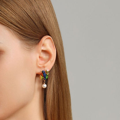Diagonal flat lay of Kingfisher Lotus Earrings with vivid enamel bird and floral elements resting against a light background.