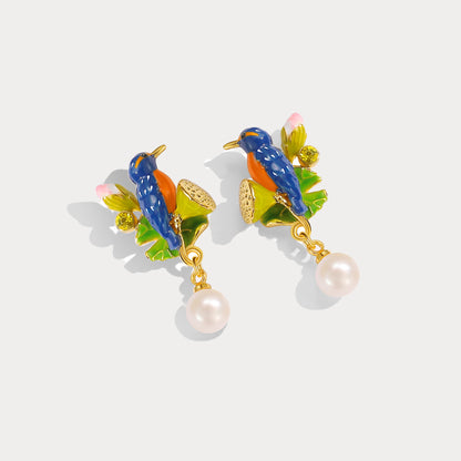 Pair of colorful enamel earrings featuring blue kingfisher birds perched on green leaves with lotus pods and pink buds, accented with pearl drops.