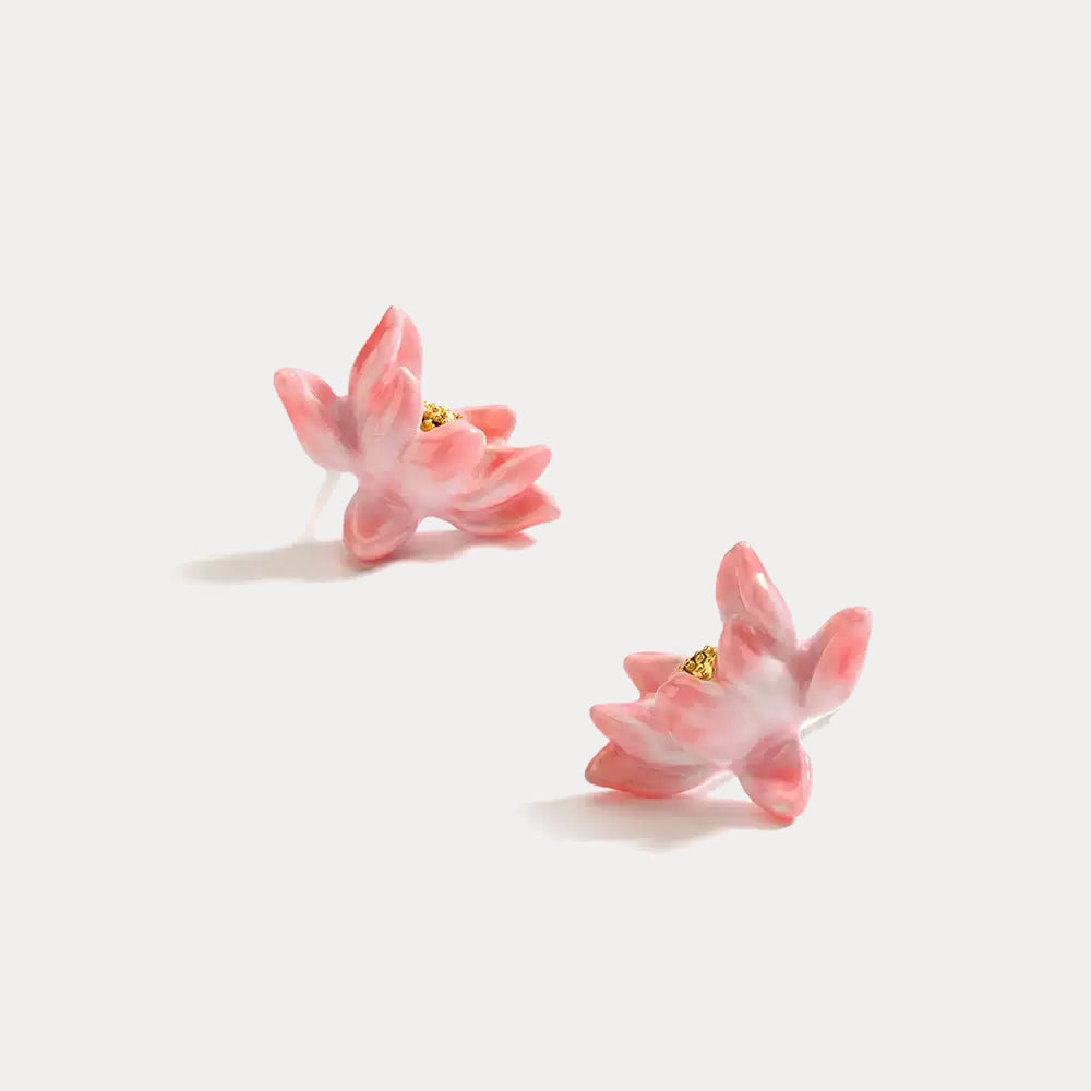 Angled view of lotus enamel earrings placed on a white surface, highlighting the petal texture and soft pink finish.