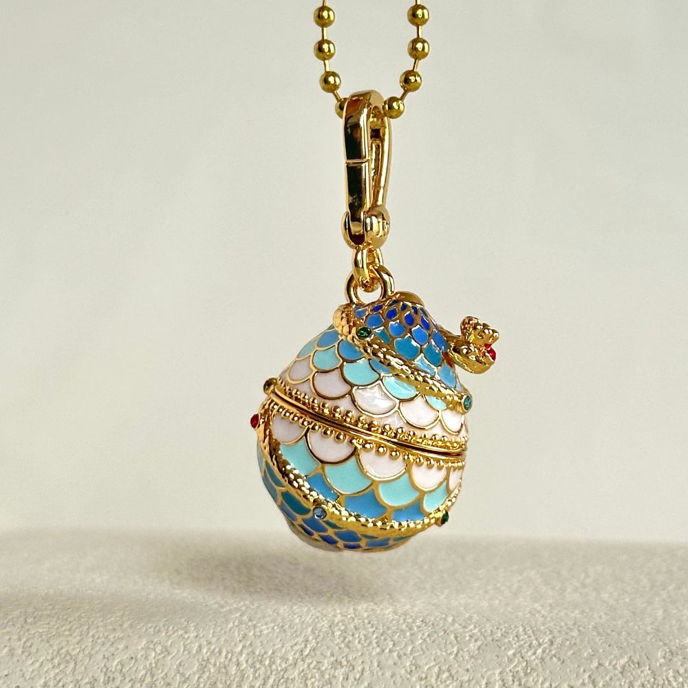 Close-up of Snake Locket Pendant shaped like a blue and white enamel egg with crown detailing and gold clasp
