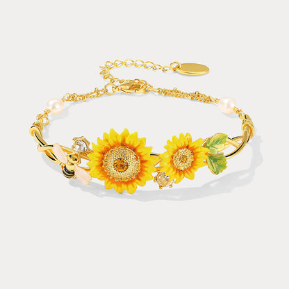 Close-up of gold sunflower cuff bracelet featuring detailed sunflowers, bee charm, and pearls on a white background
