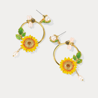 Pair of Sunflower Hoop Earrings with bee, pearl, and floral accents on flat background