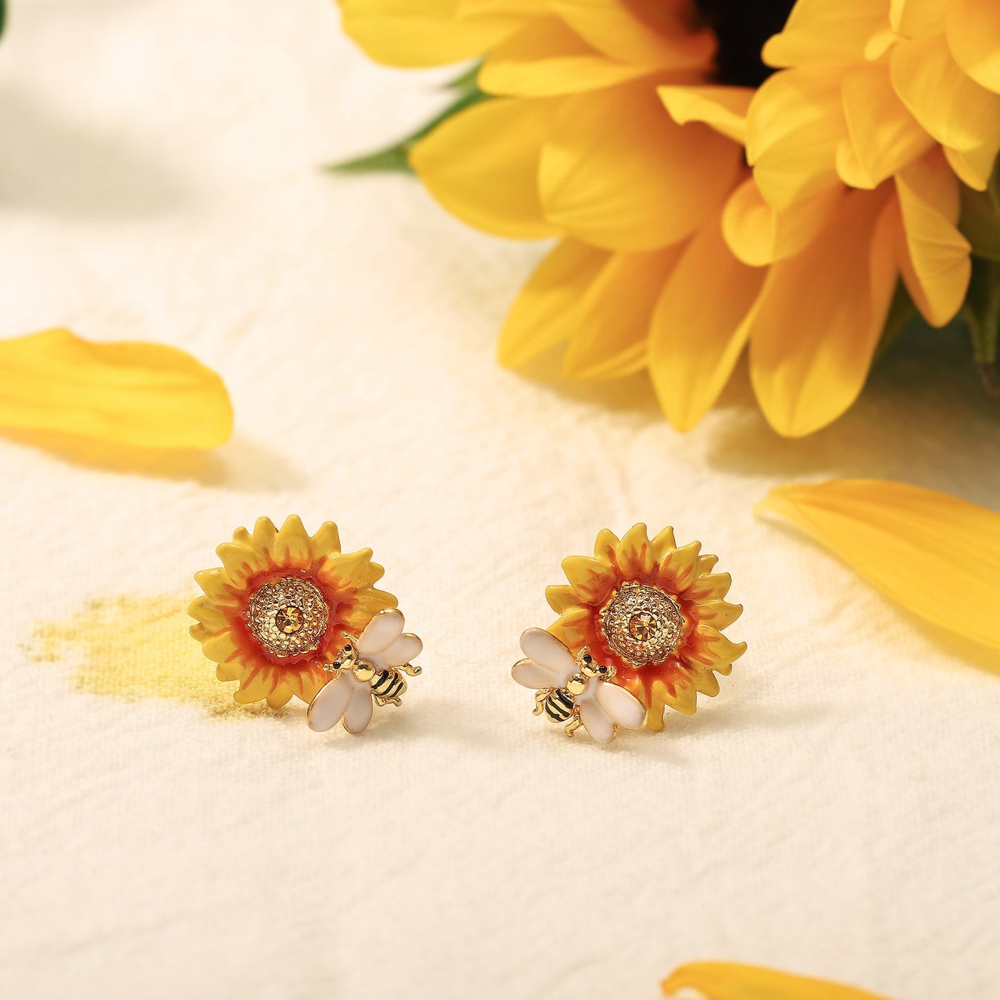 Verdivine sunflower earrings styled with real sunflower petals on a soft fabric background