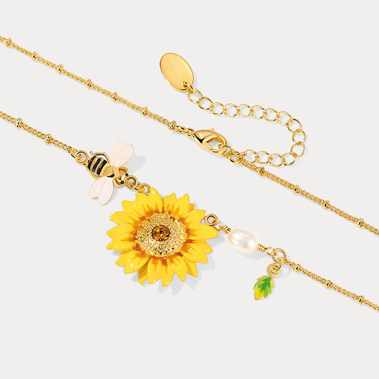 Close-up of enamel sunflower pendant with yellow petals and dangling pearl